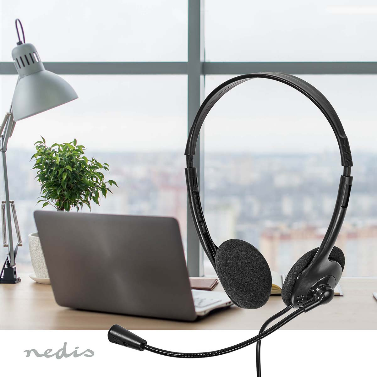 Cuffie nere con microfono su una scrivania con laptop e lampada.