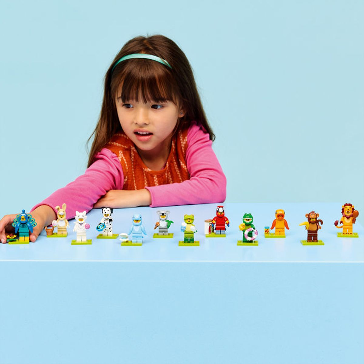 Una bambina gioca con figure Lego su un tavolo blu.