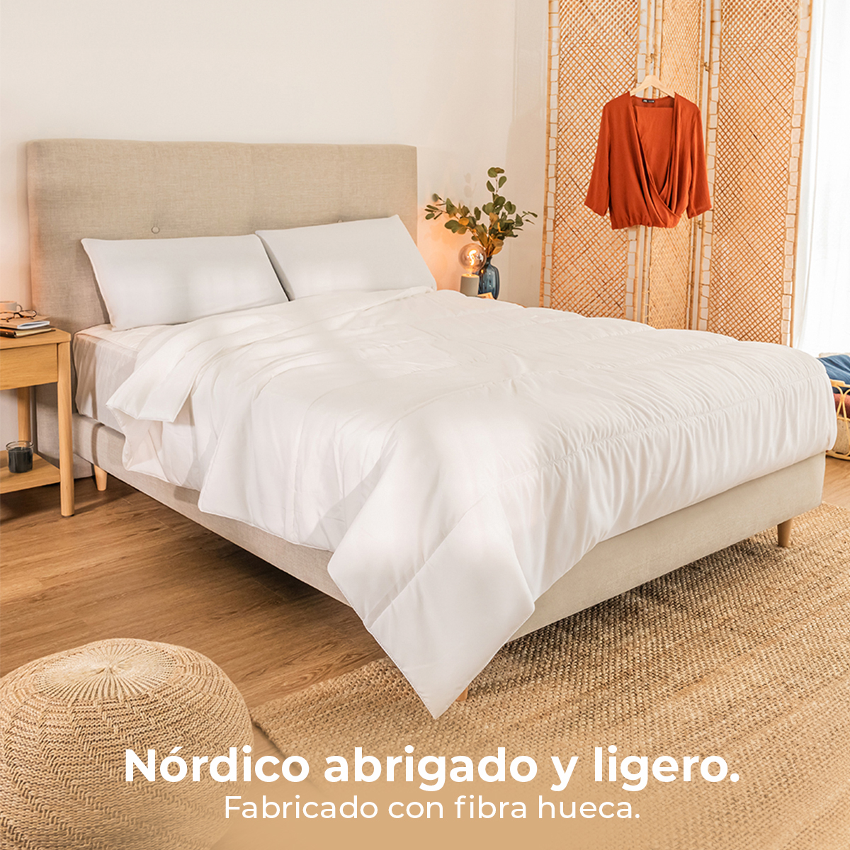 Un letto bianco con cuscini e piumone, comodino, pouf e vestiti sullo sfondo.