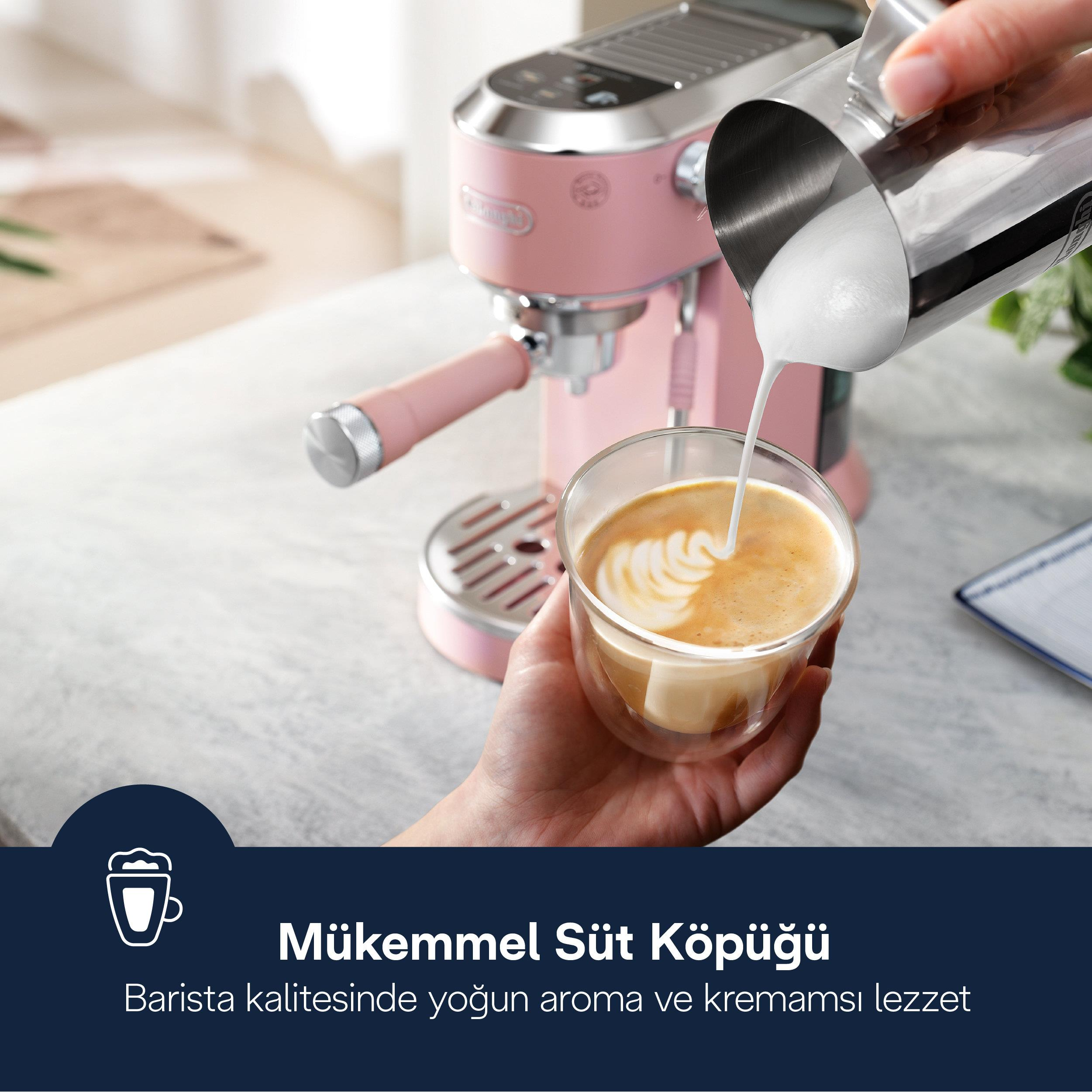 Pembe espresso makinesinin önünde bir el, kahve fincanına köpüklü süt döküyor.