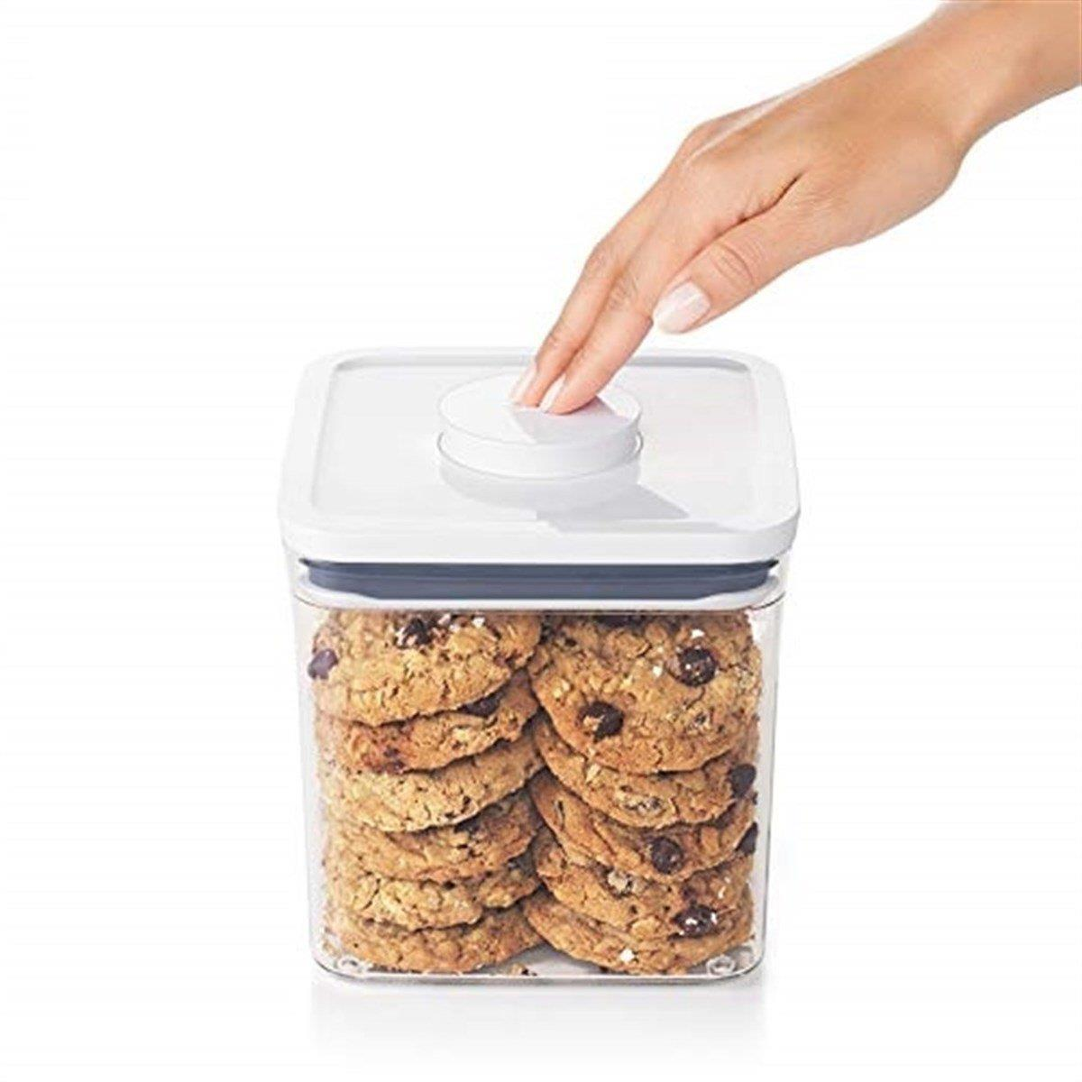 Una mano preme il pulsante di un contenitore trasparente pieno di biscotti con gocce di cioccolato.