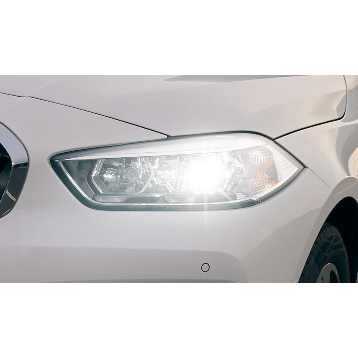 Nahaufnahme des rechten Scheinwerfers eines weißen Autos, der hell leuchtet.