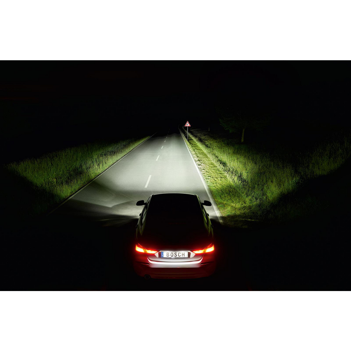 Ein Auto fährt nachts auf einer dunklen Straße, Scheinwerfer leuchten.