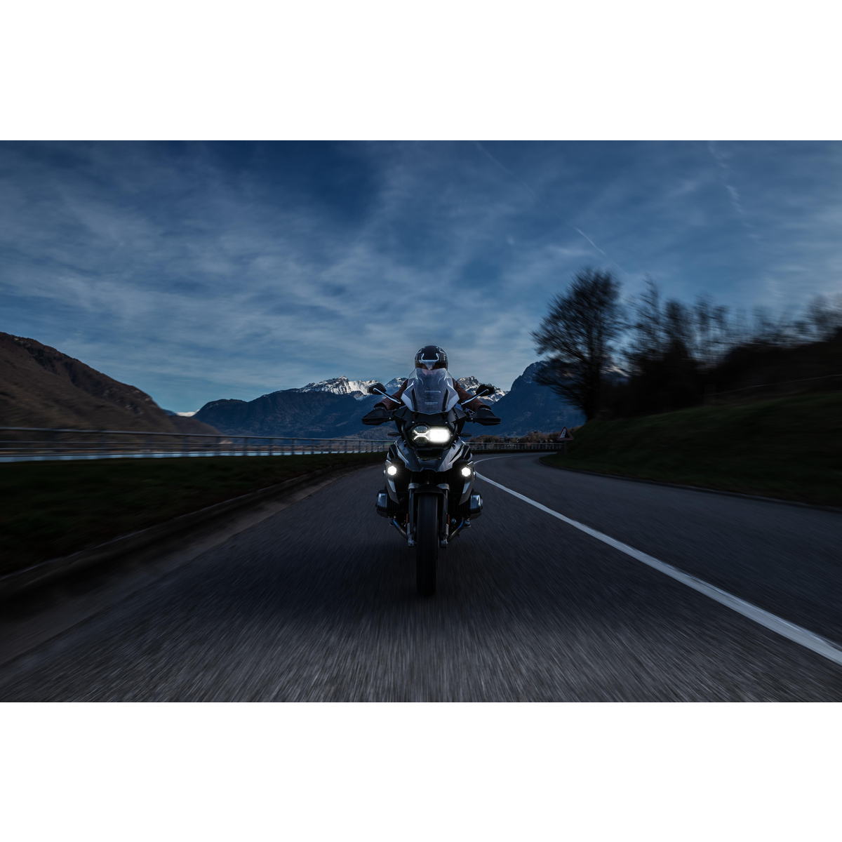 Fahrer auf einem Motorrad auf einer Straße mit Bergen und See. Abendlicht.