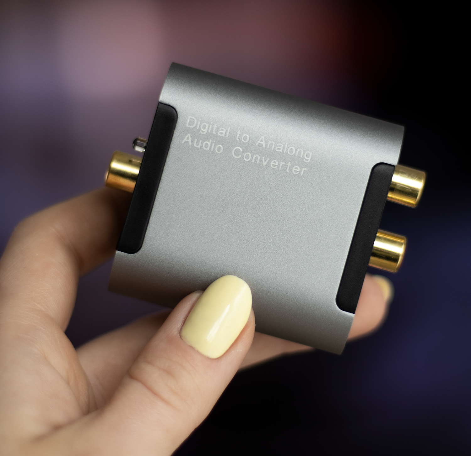 Una mano sostiene un convertidor de audio gris con conectores dorados.