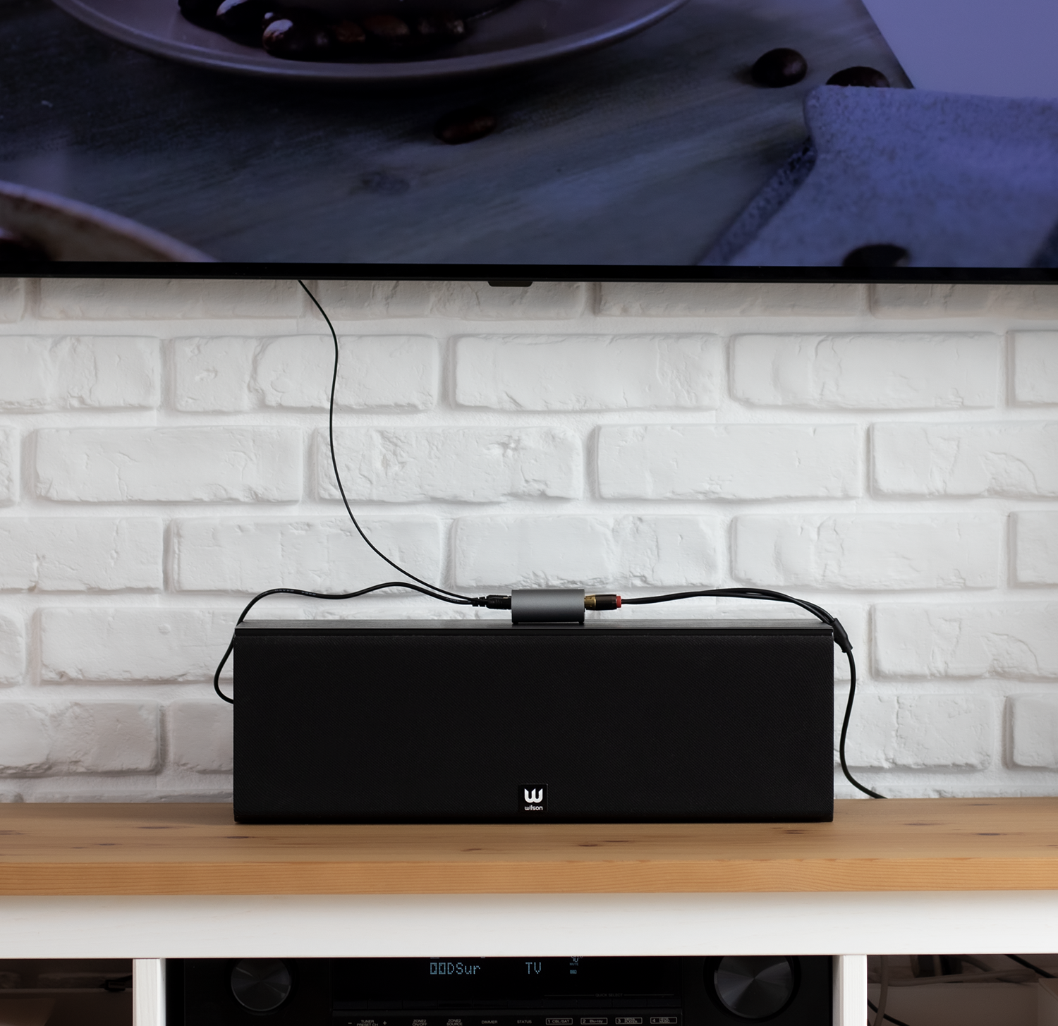 Una barra de sonido negra está en un estante de madera debajo de un televisor, conectada por cables.