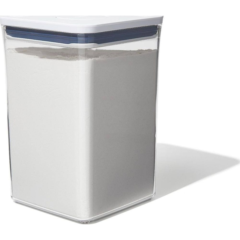 Un contenitore trasparente pieno di polvere bianca con coperchio blu e bianco.