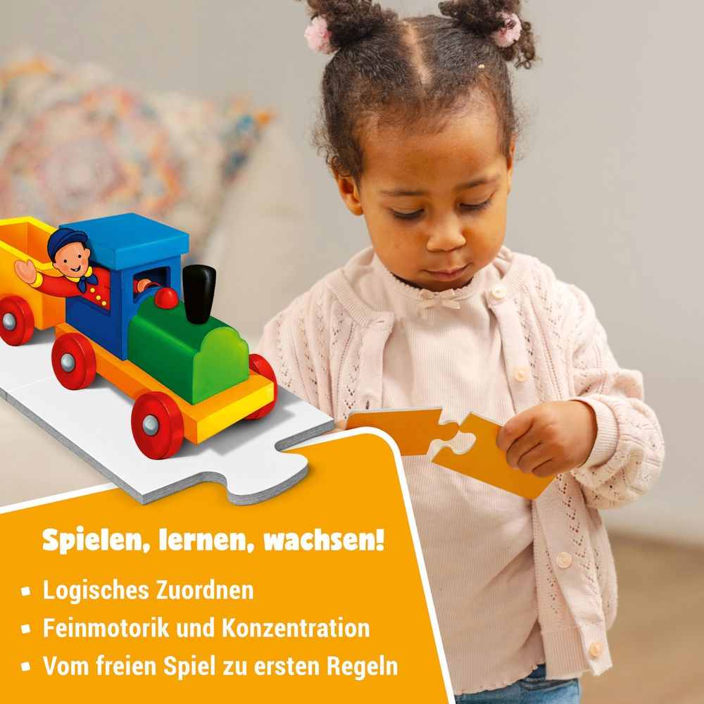 Una bambina costruisce un trenino giocattolo di legno colorato e tiene un pezzo di puzzle.