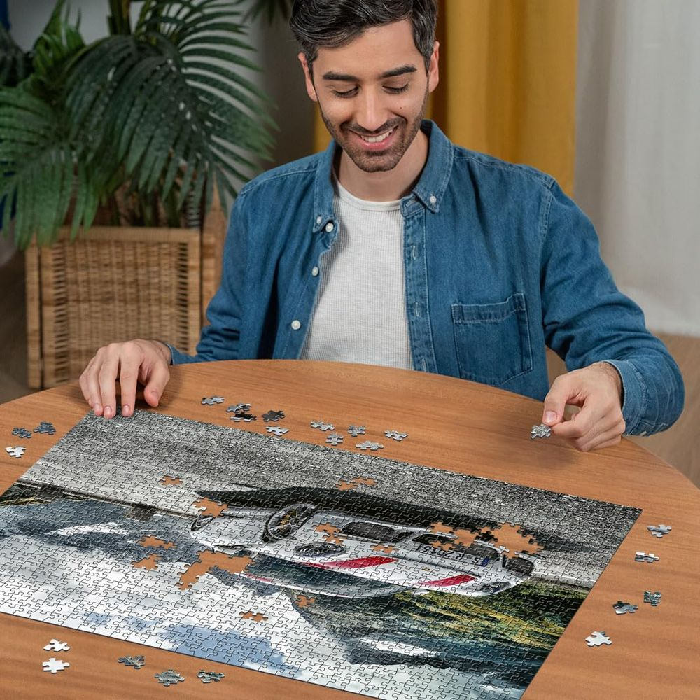 Mann baut ein Puzzle mit einem Auto. Er hält ein Puzzleteil in der Hand.
