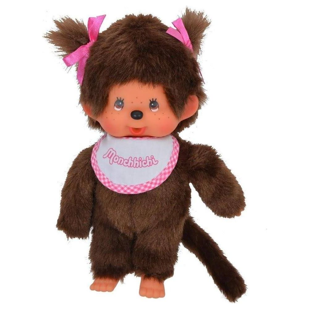 Eine braune Monchhichi-Puppe mit rosa Schleifen und einem Lätzchen steht auf weißem Grund.
