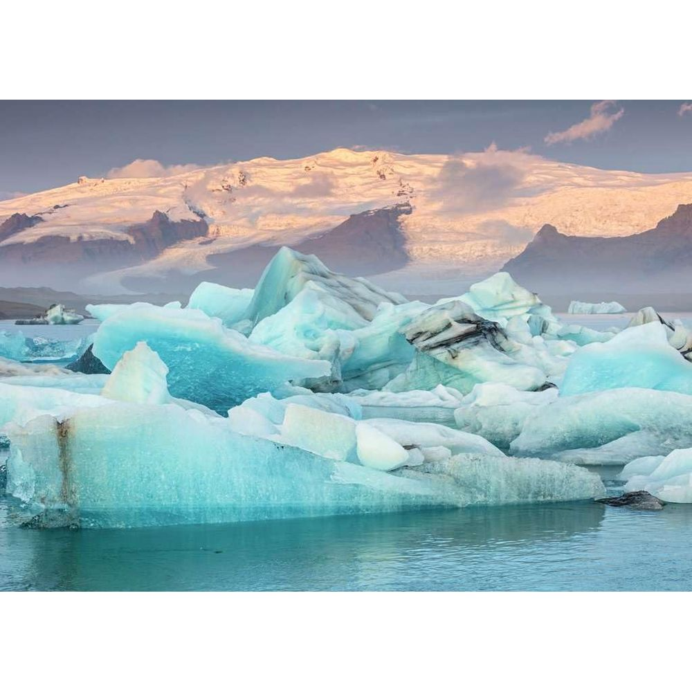 Des icebergs flottent dans l'eau bleue devant des montagnes enneigées.