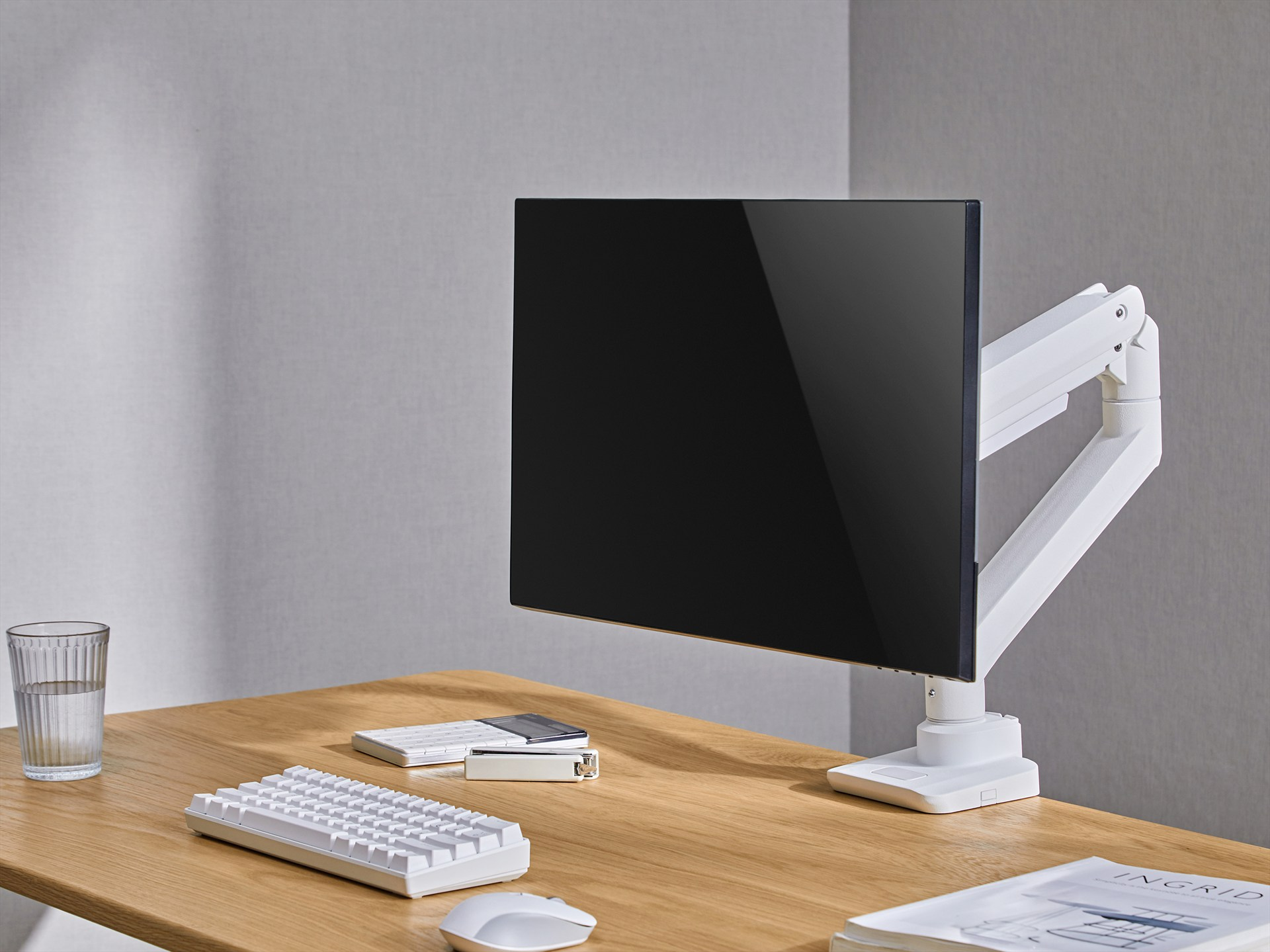 Ein moderner Schreibtisch mit einem schwarzen Monitor auf einem weißen Arm, Tastaturen, Maus und Glas Wasser.