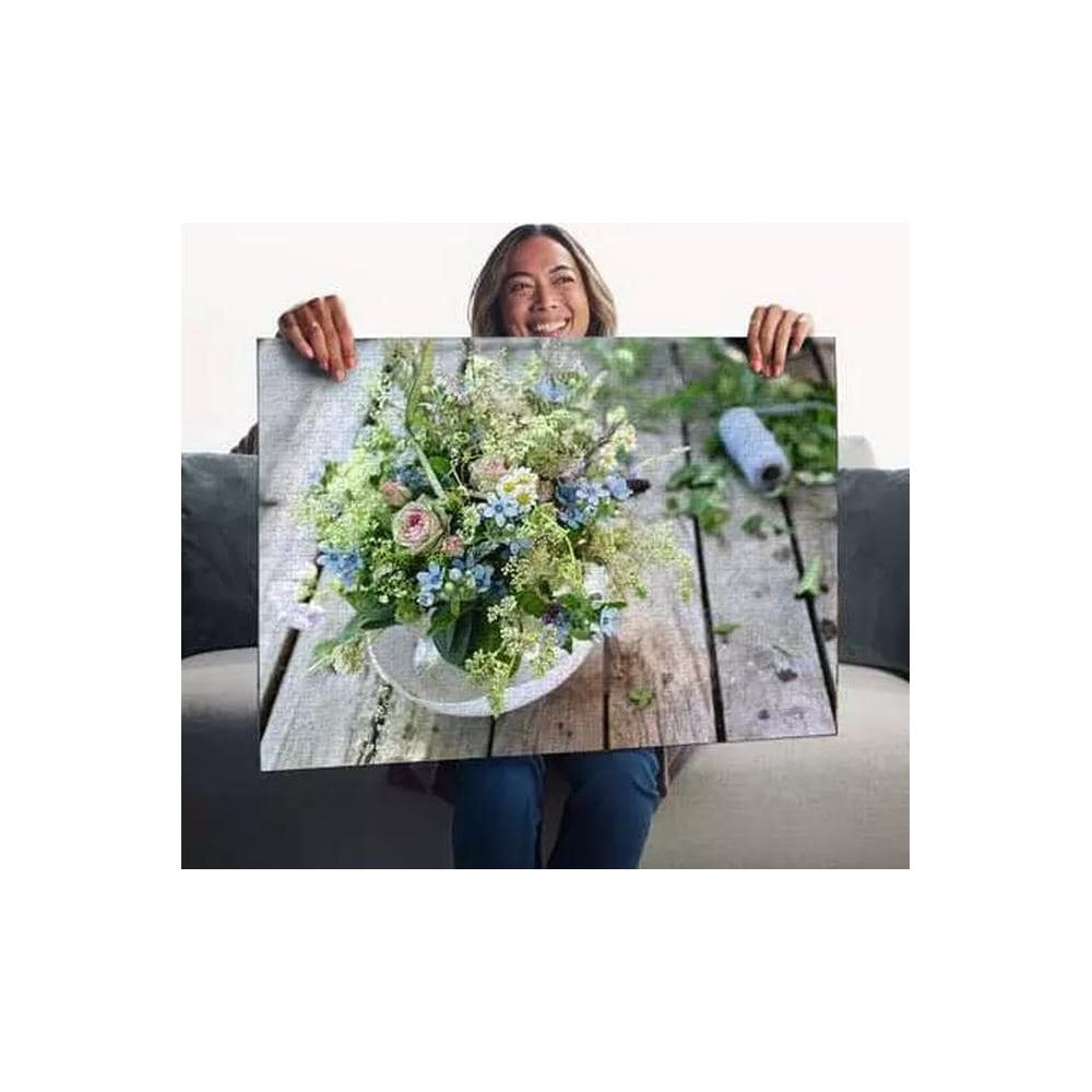 Frau hält ein Puzzle eines Blumenstraußes auf Holztisch mit Garnrolle.
