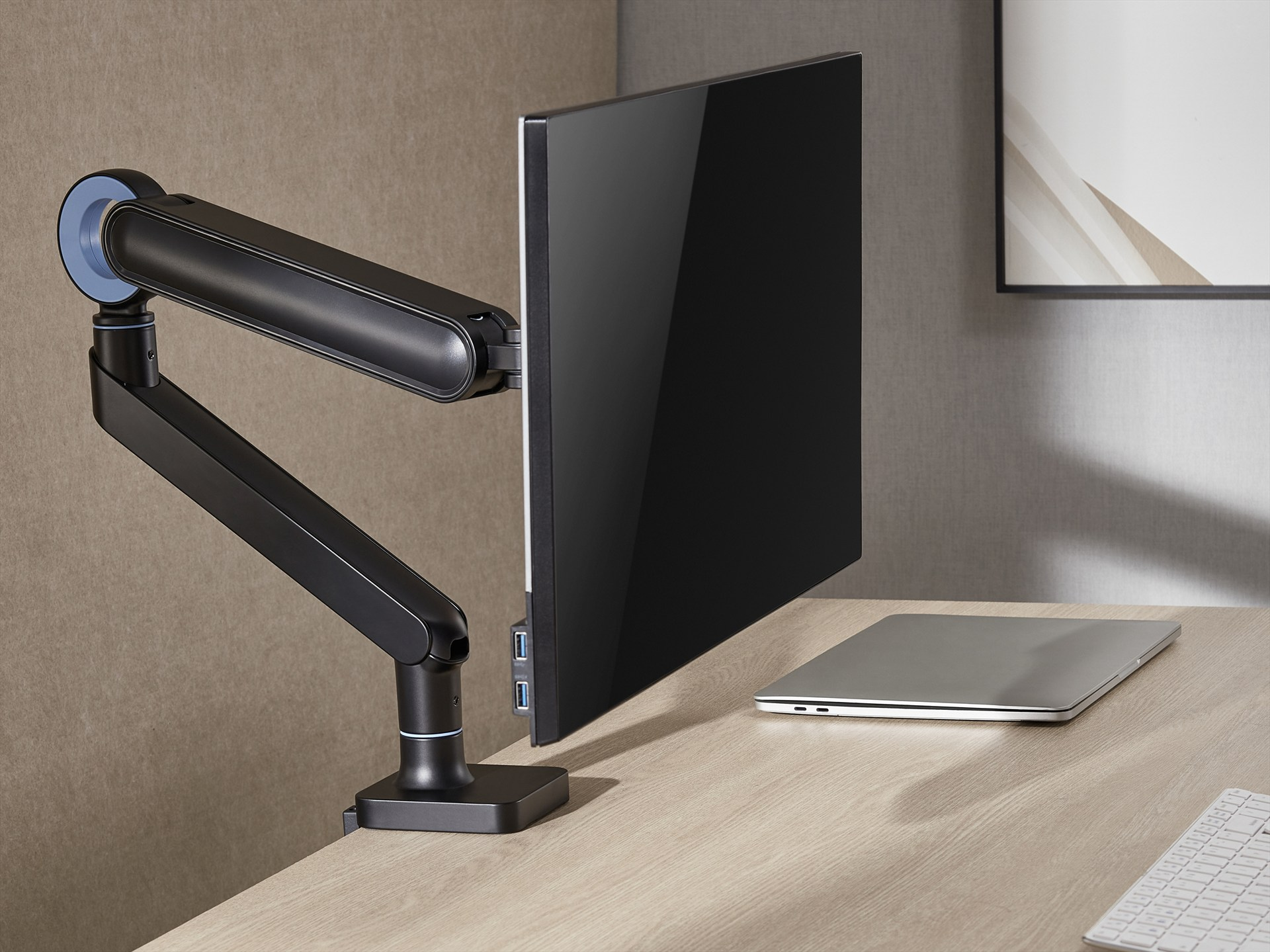 Ein schwarzer Monitorarm hält einen schwarzen Monitor über einem Schreibtisch mit Laptop und Tastatur.