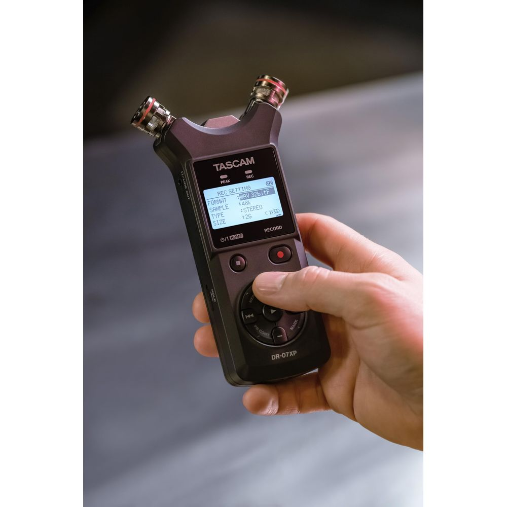 Dłoń trzyma czarny rejestrator Tascam DR-07XP z mikrofonami.