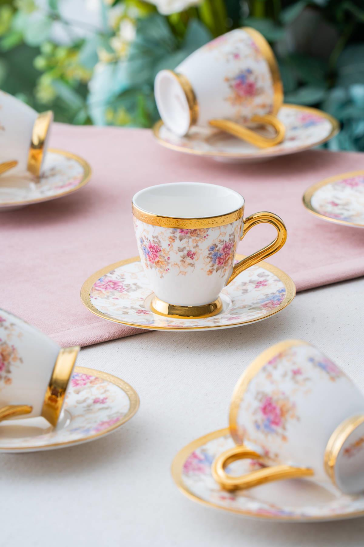 Altın kulplu ve çiçek desenli beyaz espresso fincanları, tabaklarıyla birlikte.