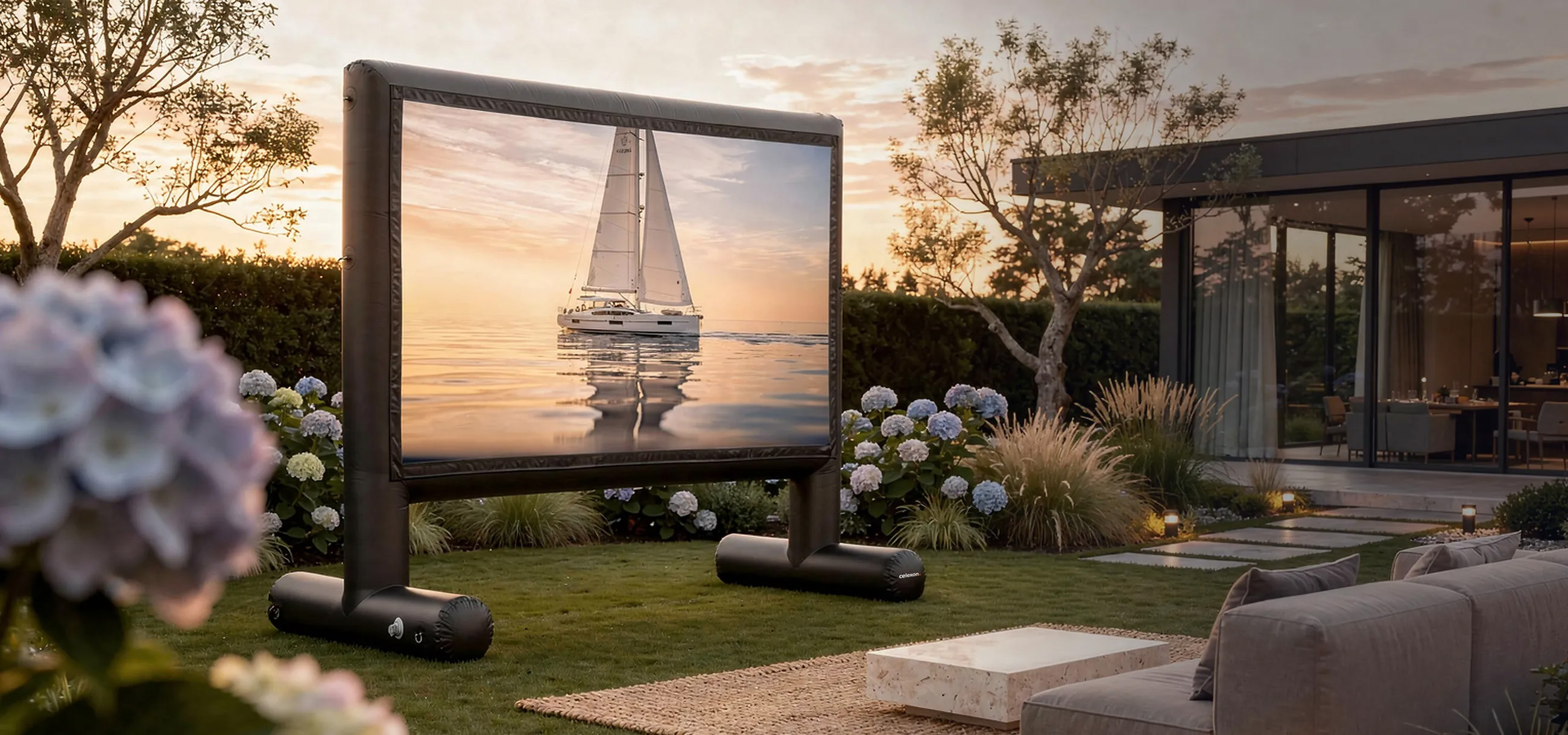 Aufblasbarer Bildschirm im Garten mit Segelboot-Bild, daneben Blumen und Haus.