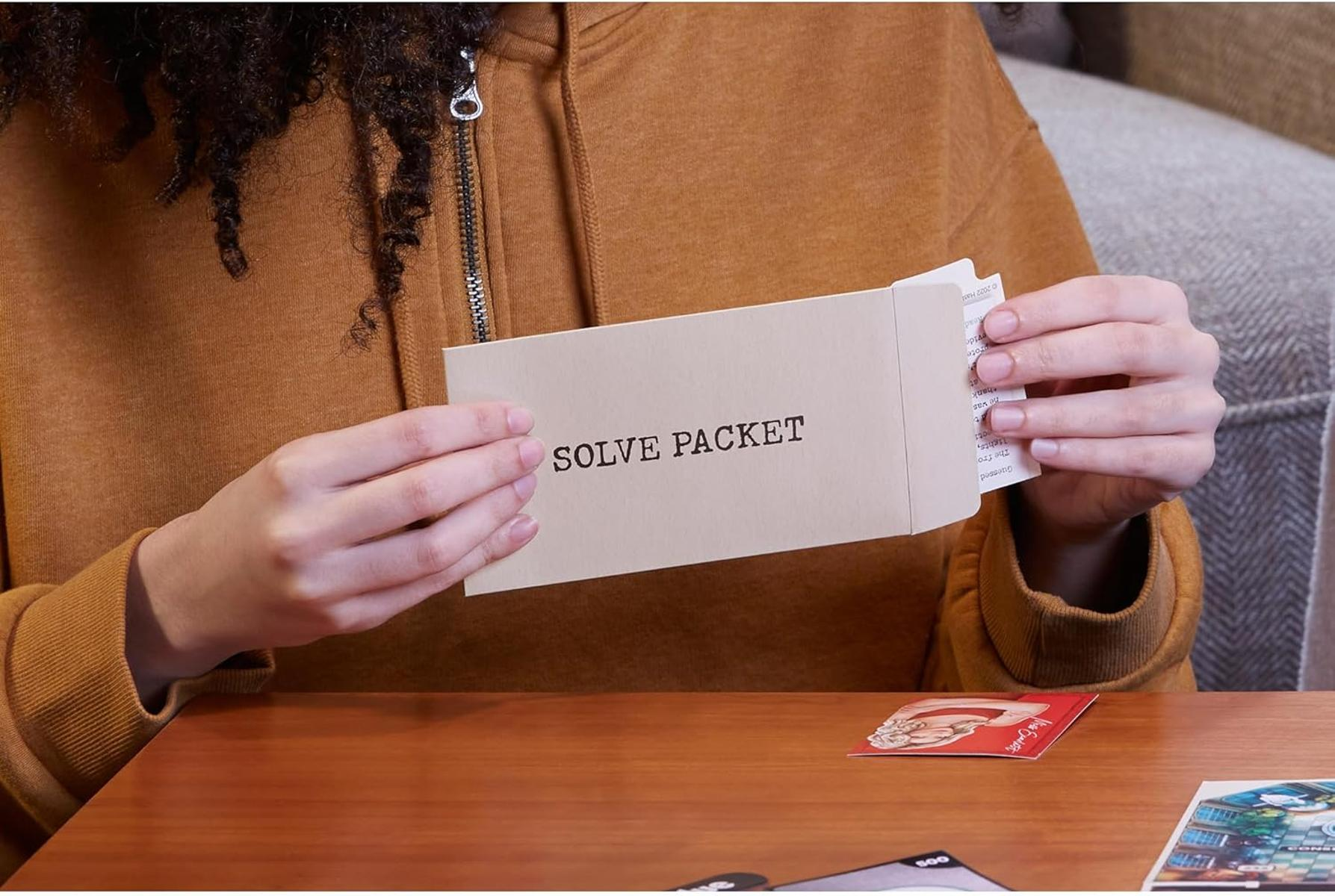 Person öffnet ein "Solve Packet" auf einem Holztisch mit Spielkarten.