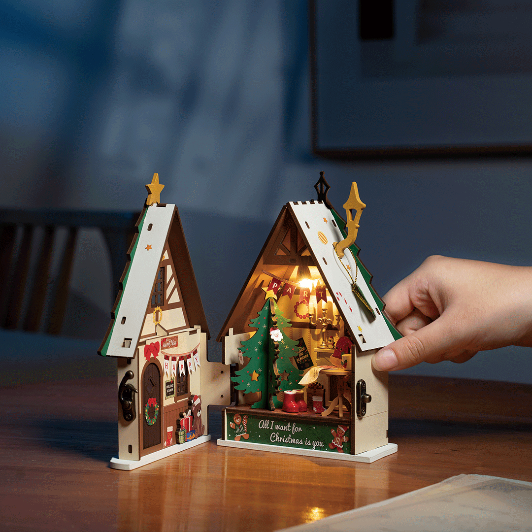 Un diorama natalizio in legno con luci, alberi e una mano che lo chiude.