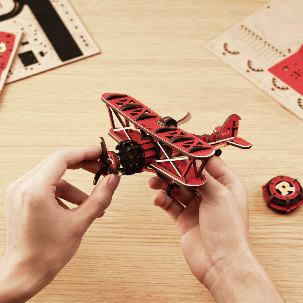 Mani tengono un modello di aeroplano in legno rosso su superficie di legno.