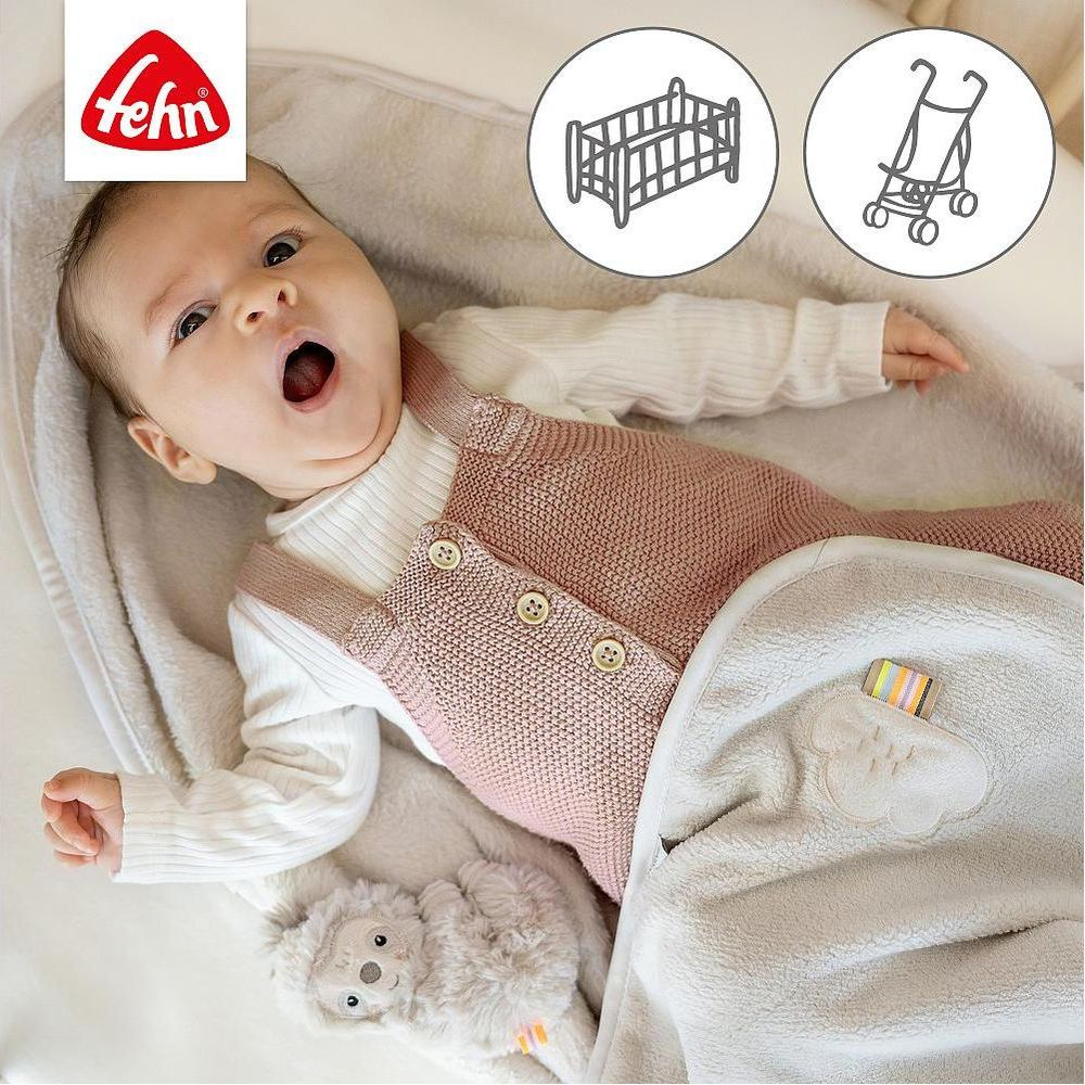 Baby in rosa Latzhose gähnt, liegt auf Decke mit Plüschtier. Fehn-Logo, Gitterbett & Kinderwagen-Icons.