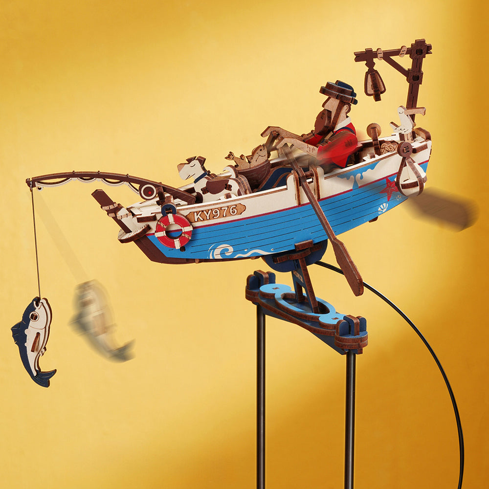 Maquette en bois d'un bateau de pêche avec un homme, un chien et un poisson sur fond jaune.