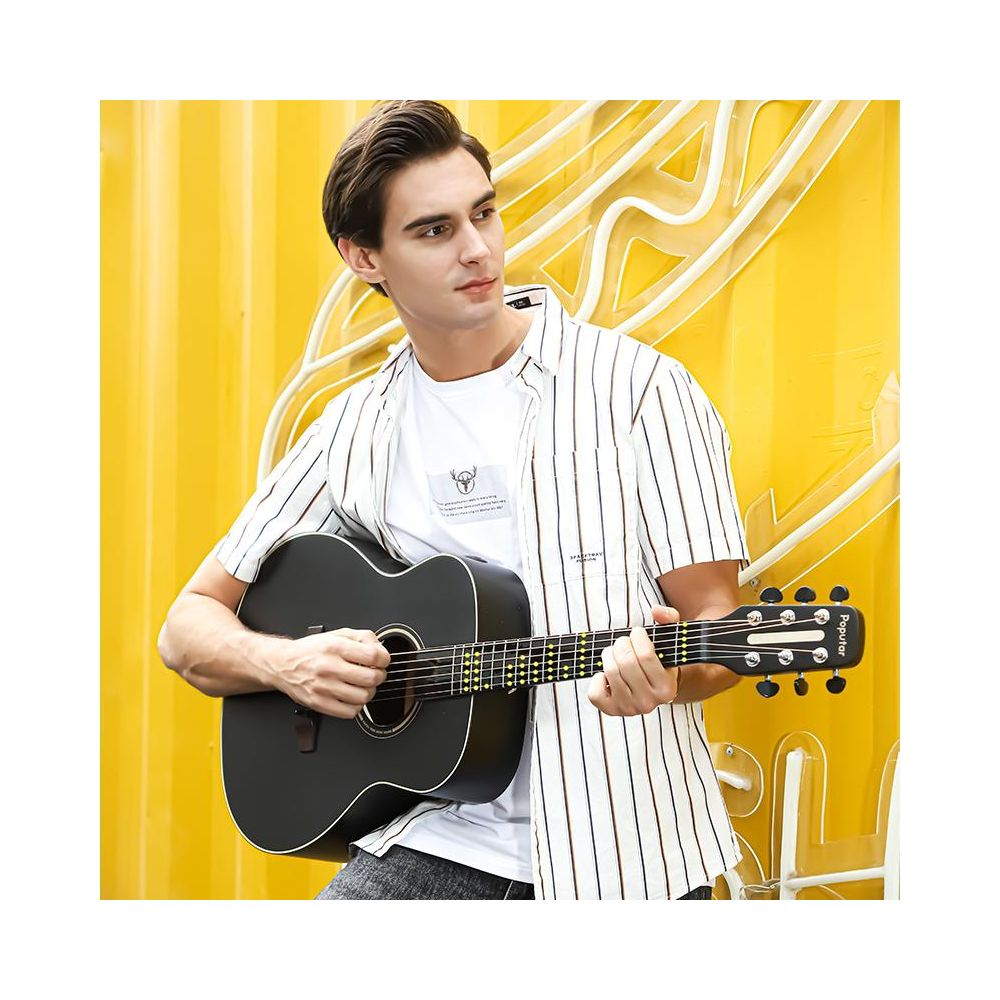 Un homme joue d'une guitare noire devant un mur jaune orné de lignes blanches.