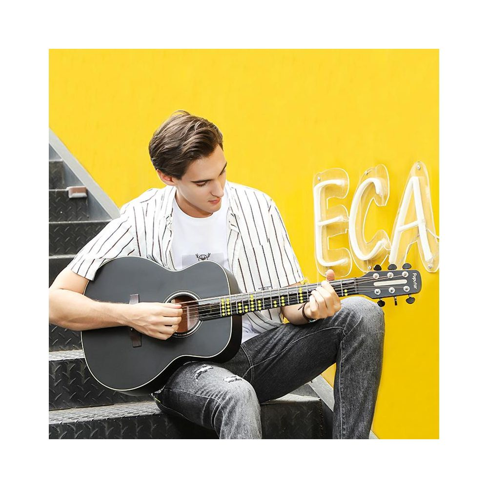 Un homme assis sur des escaliers joue d'une guitare noire devant un mur jaune.