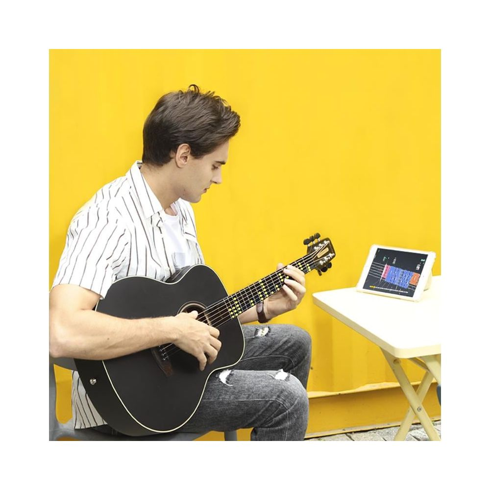 Un homme joue de la guitare devant un mur jaune, avec une tablette à côté.