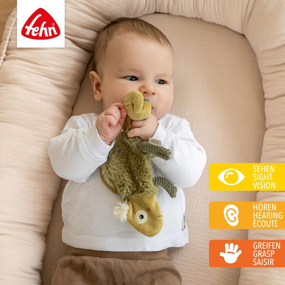 Ein Baby liegt in einem Nest und hält ein grünes Plüschtier.