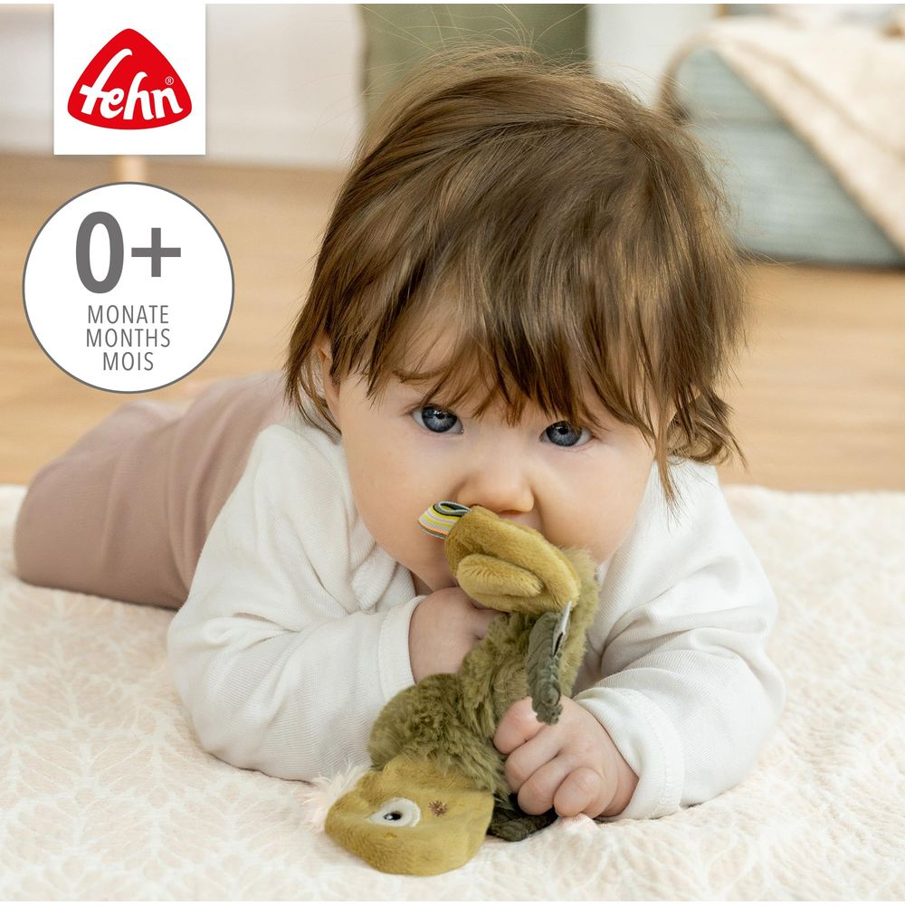 Ein Baby liegt auf dem Bauch und kaut auf einem Stofftier. Oben links ist das Fehn-Logo.