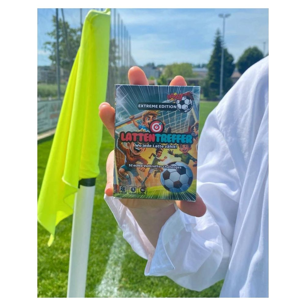 Persona tiene gioco di carte calcio 'Latten Treffer Extreme Edition' vicino a campo calcio.