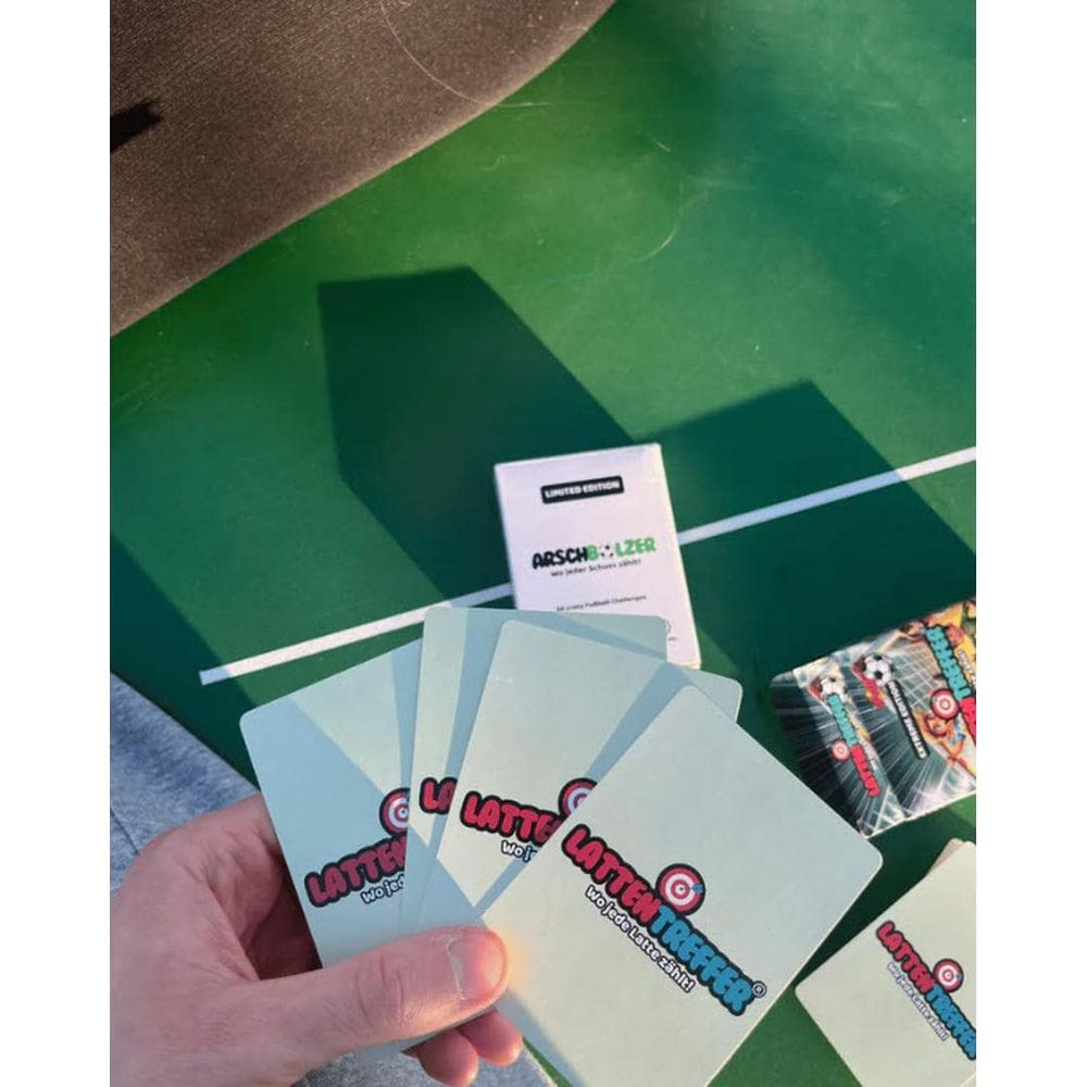 Una mano tiene carte con scritte come "Latten Treffer" su sfondo verde.