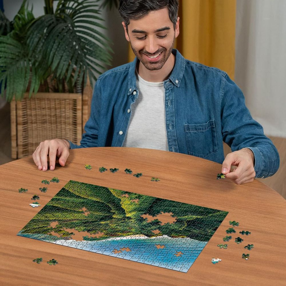 Mann sitzt an einem Holztisch und legt ein Puzzle eines tropischen Strandes zusammen.