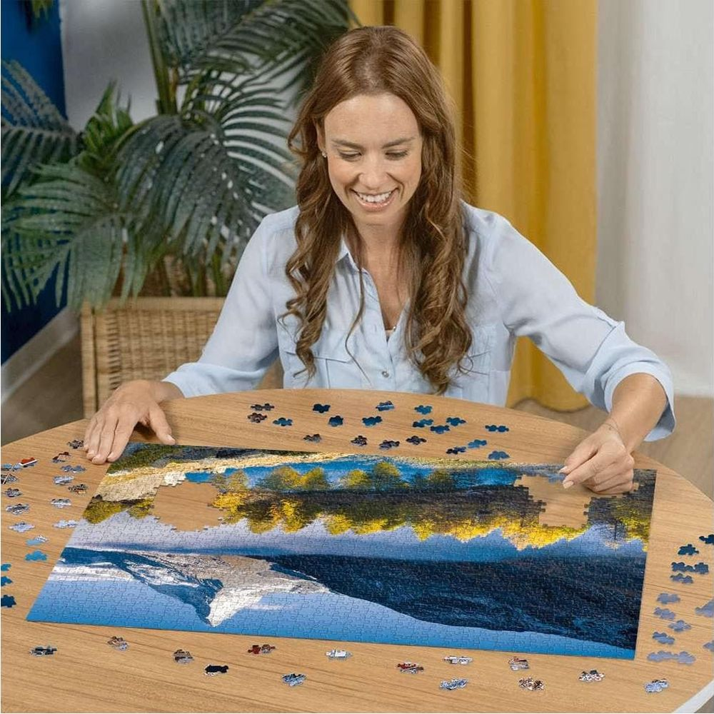 Donna compone puzzle di riflesso montano in lago su tavolo legno.