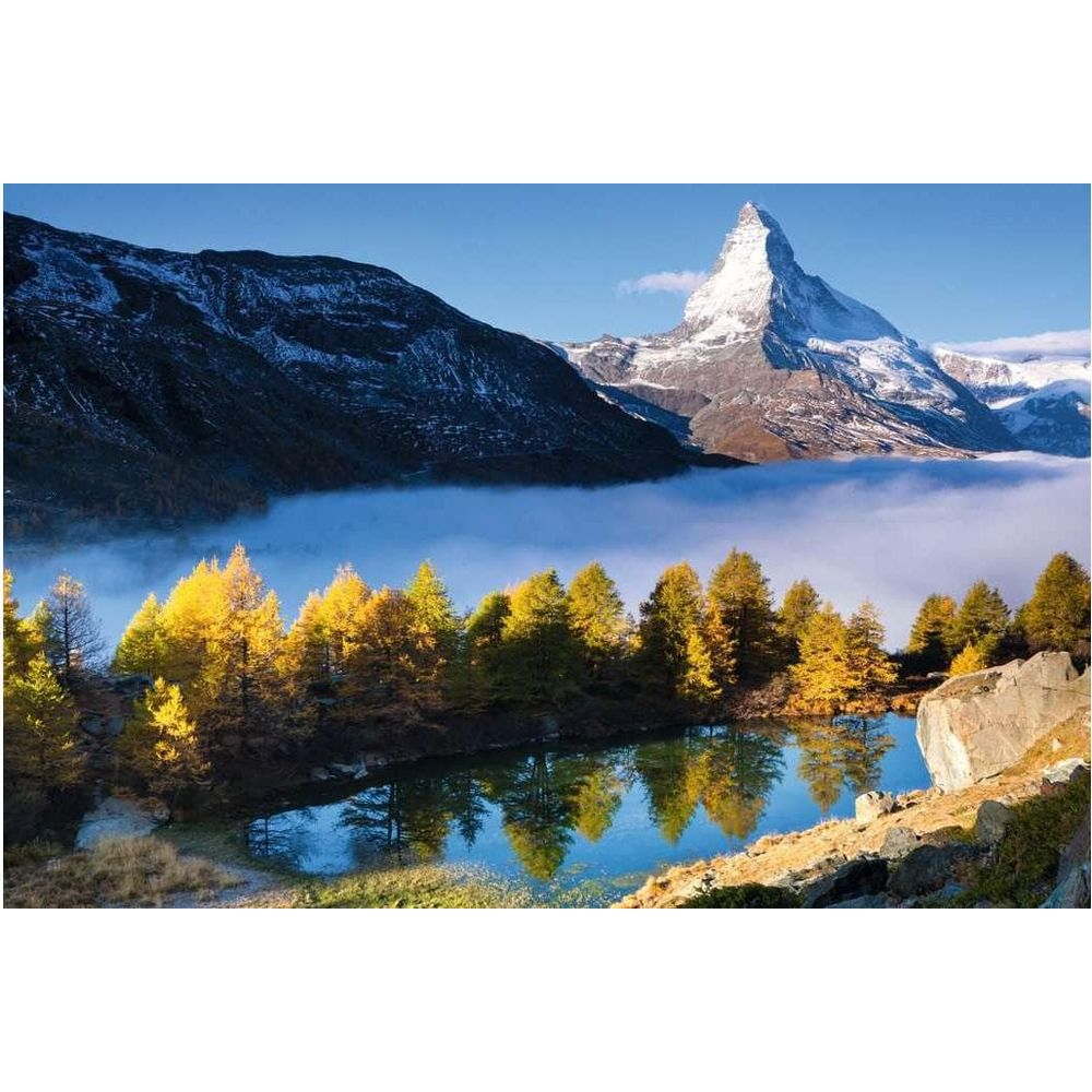 Lago di montagna con alberi gialli e sfondo montuoso nebbioso.