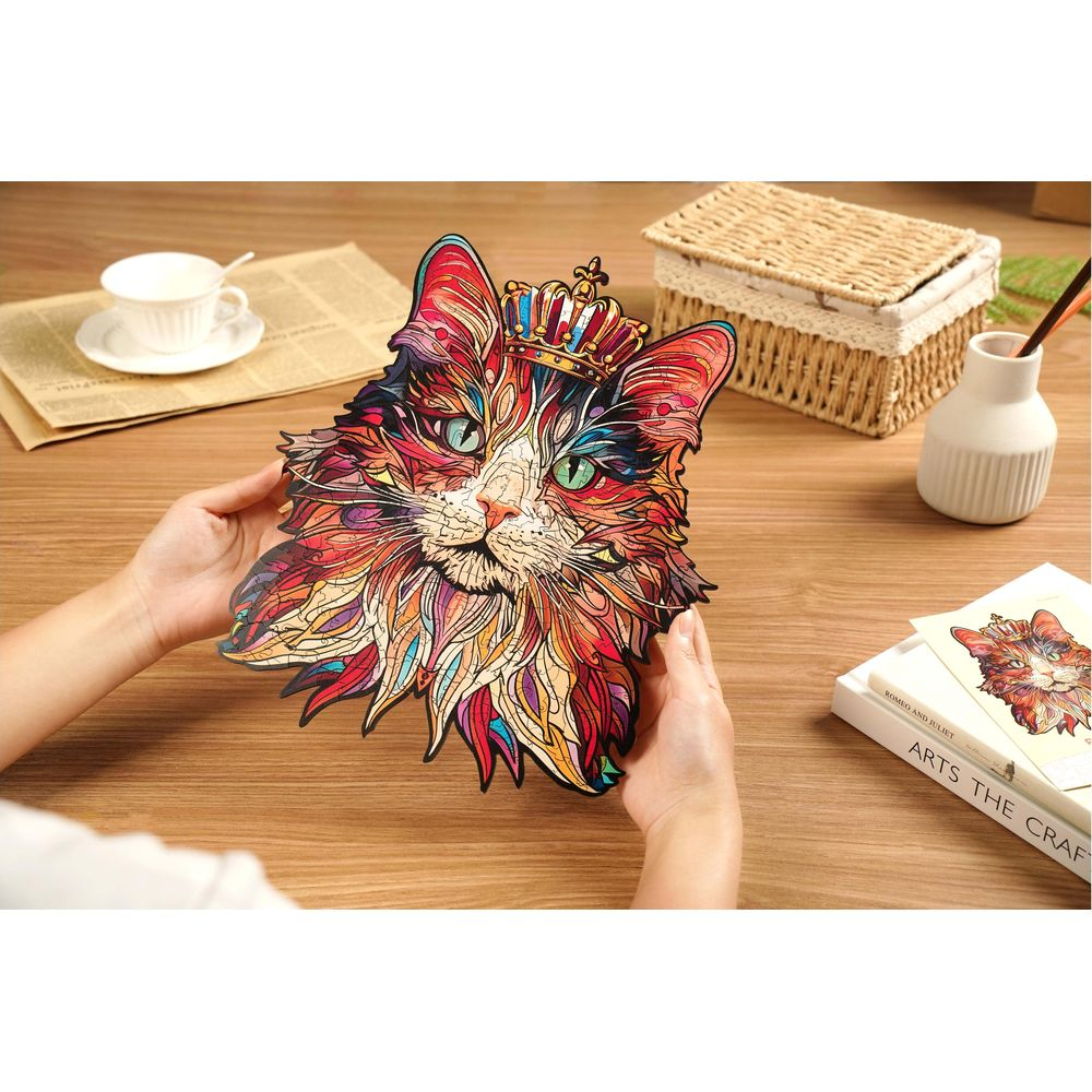 Bunte Katzenpuzzle mit Krone wird von Händen gehalten, auf einem Holztisch.