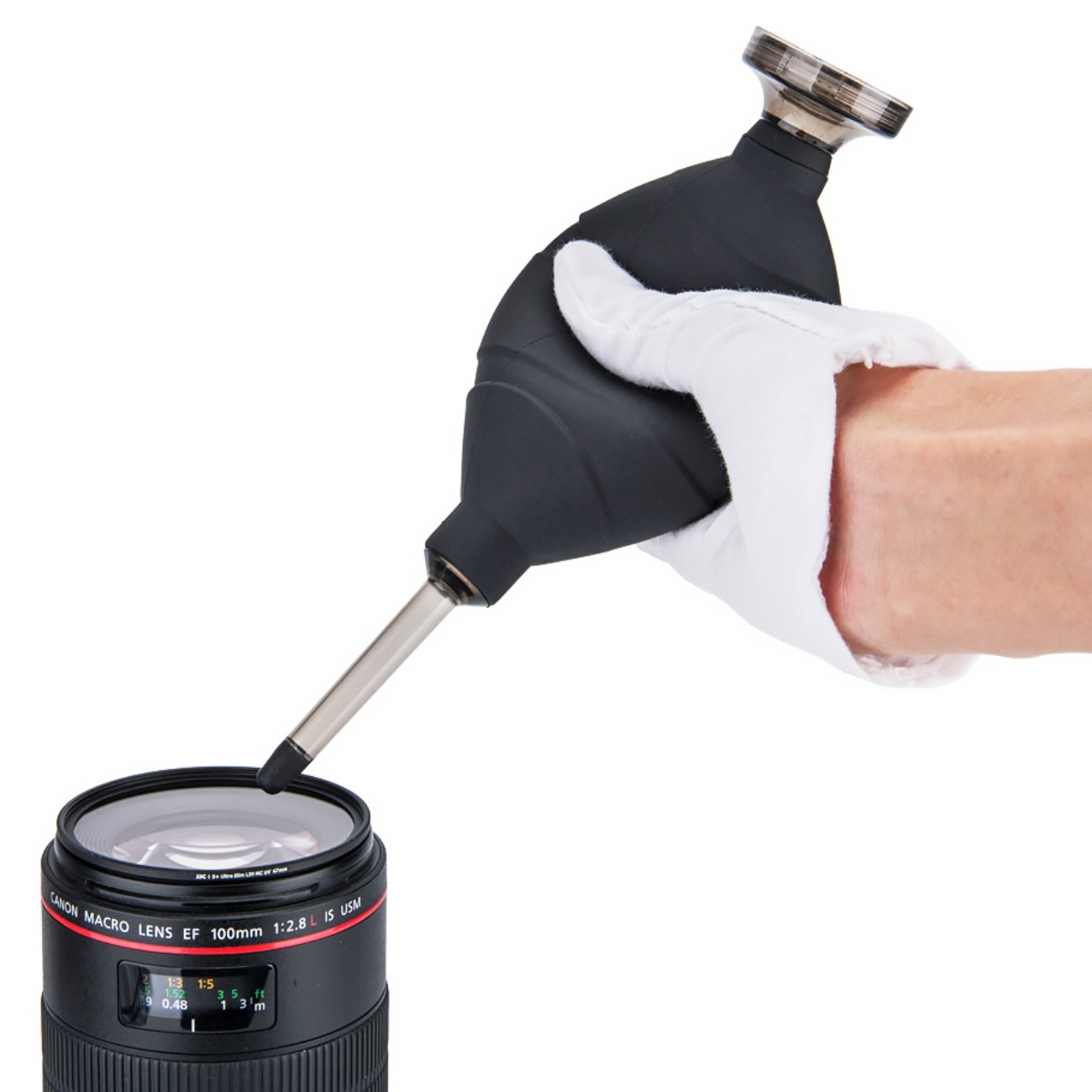 Eine Hand in einem weißen Handschuh benutzt einen schwarzen Blasebalg, um eine Canon-Makrolinse zu reinigen.