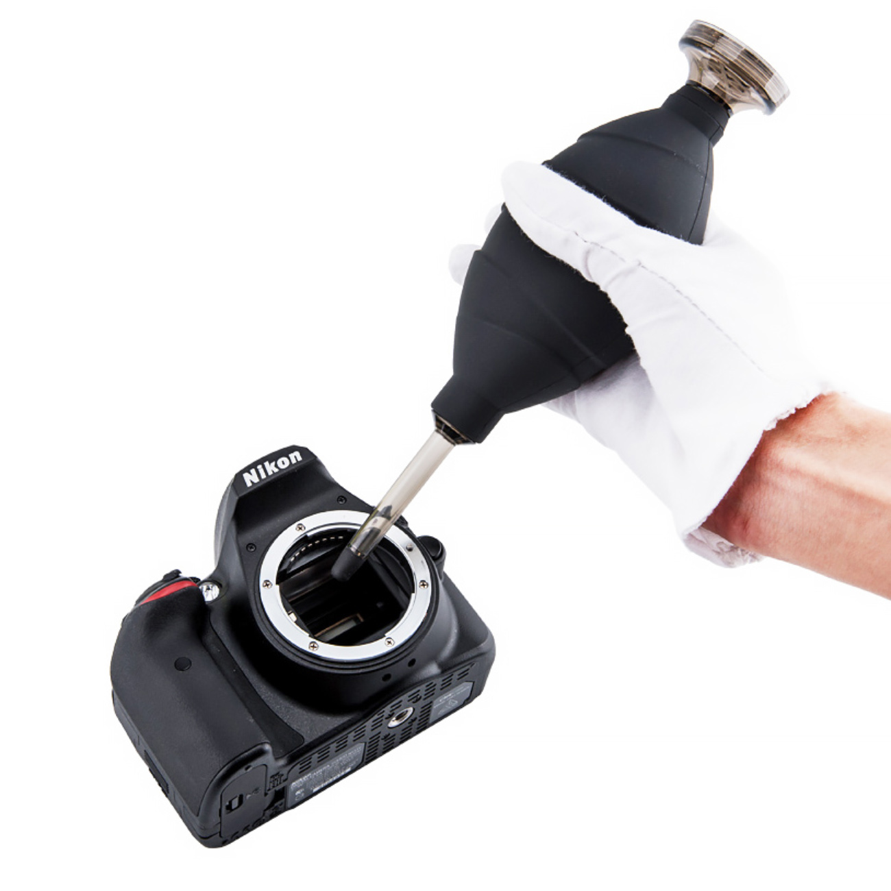 Eine behandschuhte Hand benutzt einen schwarzen Blasebalg zur Reinigung eines Nikon-Kamerasensors.