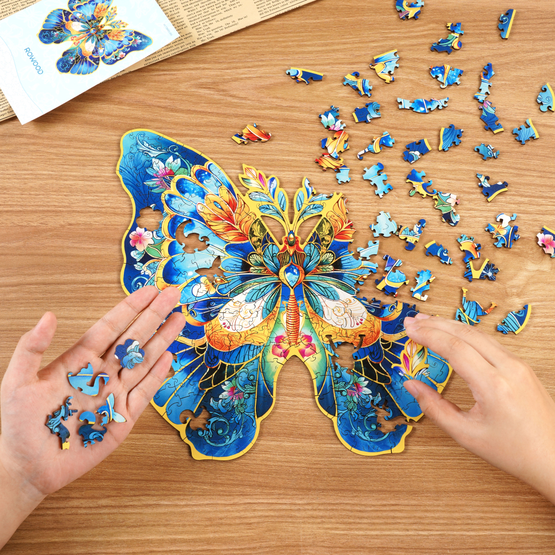Hände setzen Puzzleteile zu einem blauen Schmetterling auf einem Holztisch.