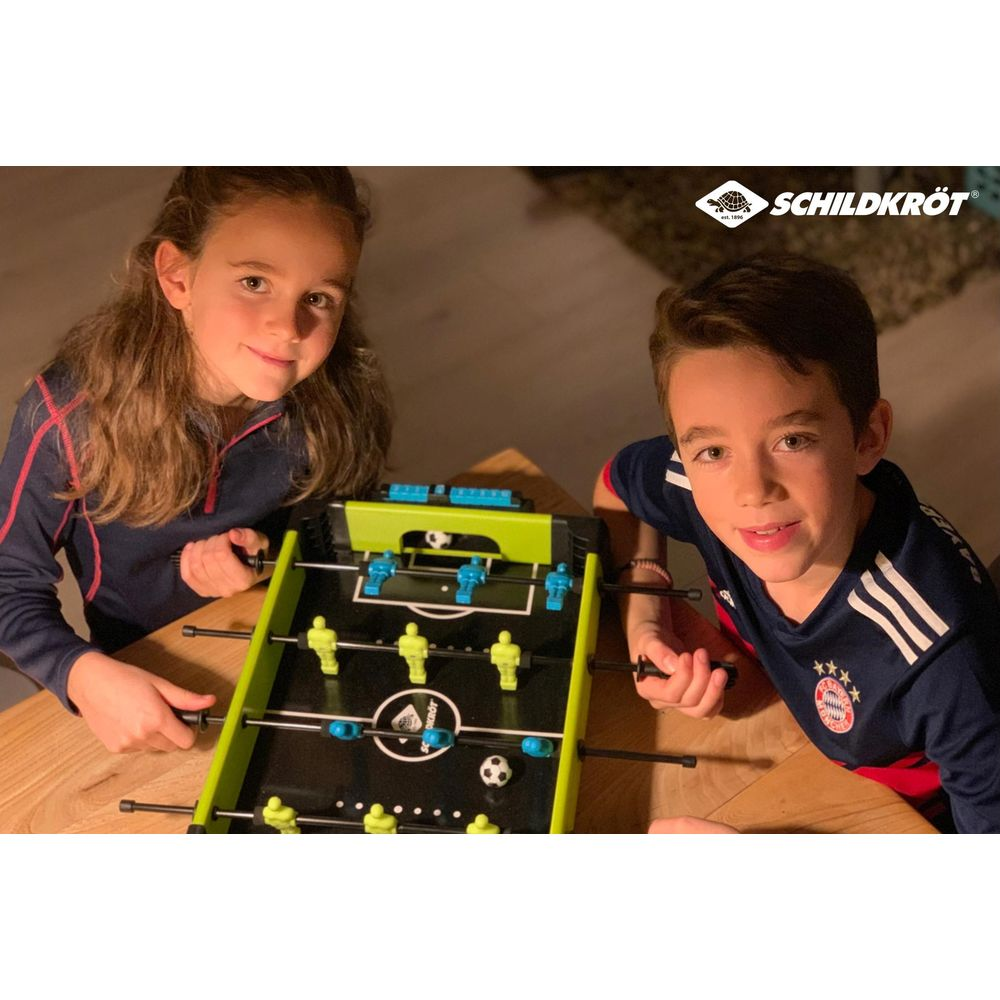 Due bambini giocano a calcio balilla. Una bambina e un bambino sono seduti a un tavolo.