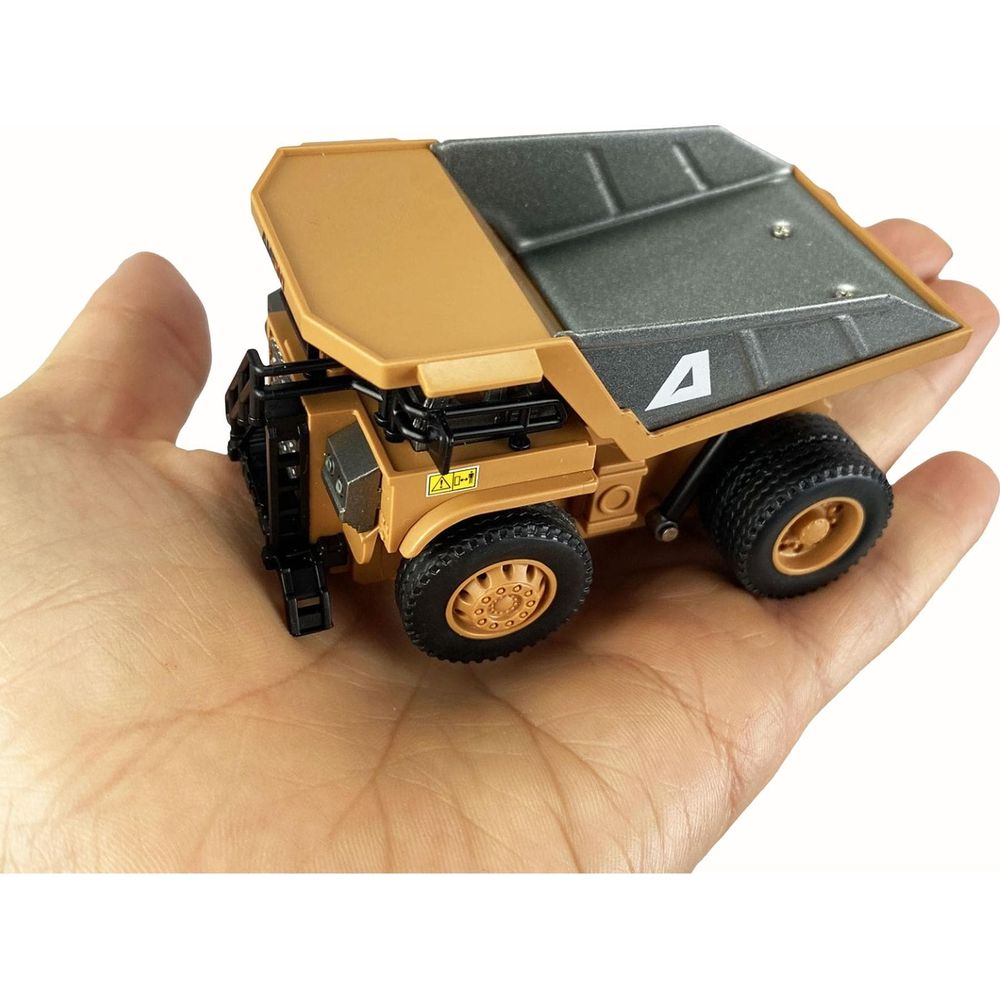 Petit camion benne jouet jaune avec benne noire, tenu dans une main.
