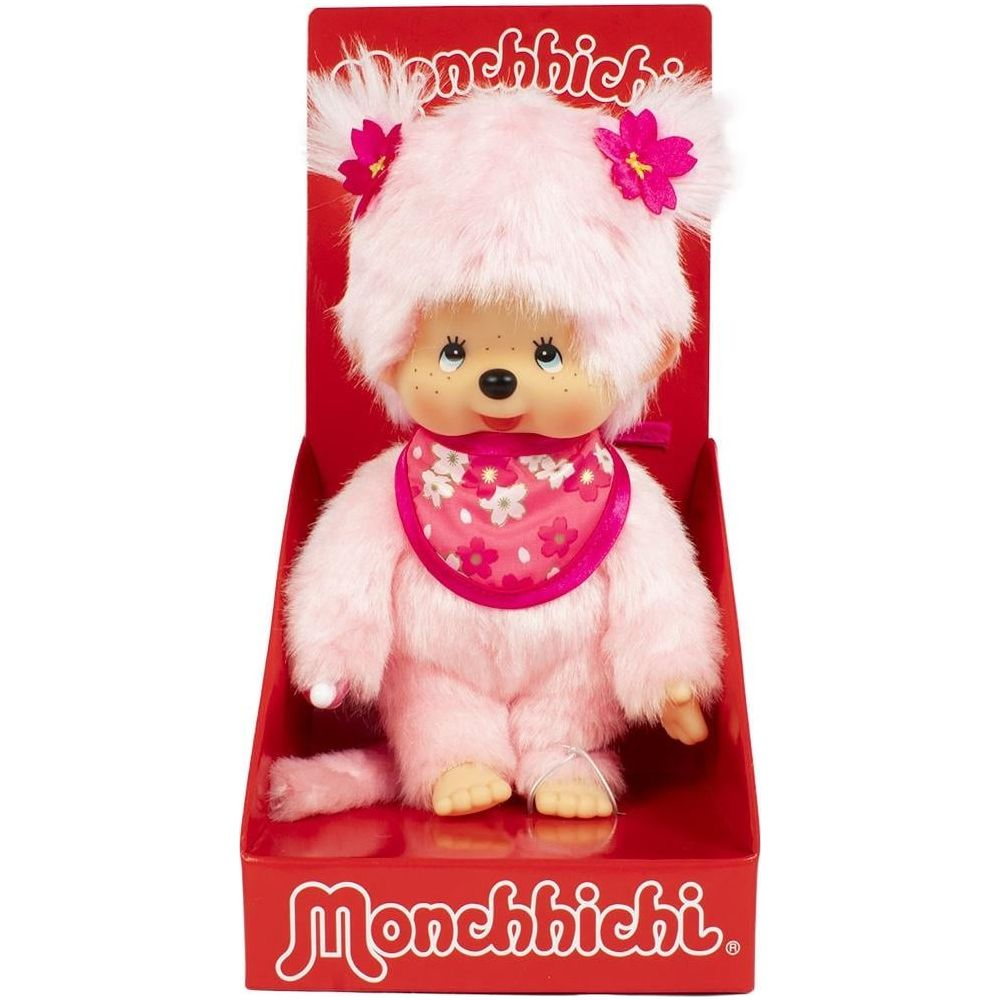 Ein rosafarbener Monchhichi mit Lätzchen und Blumenapplikationen in einer roten Verpackung.