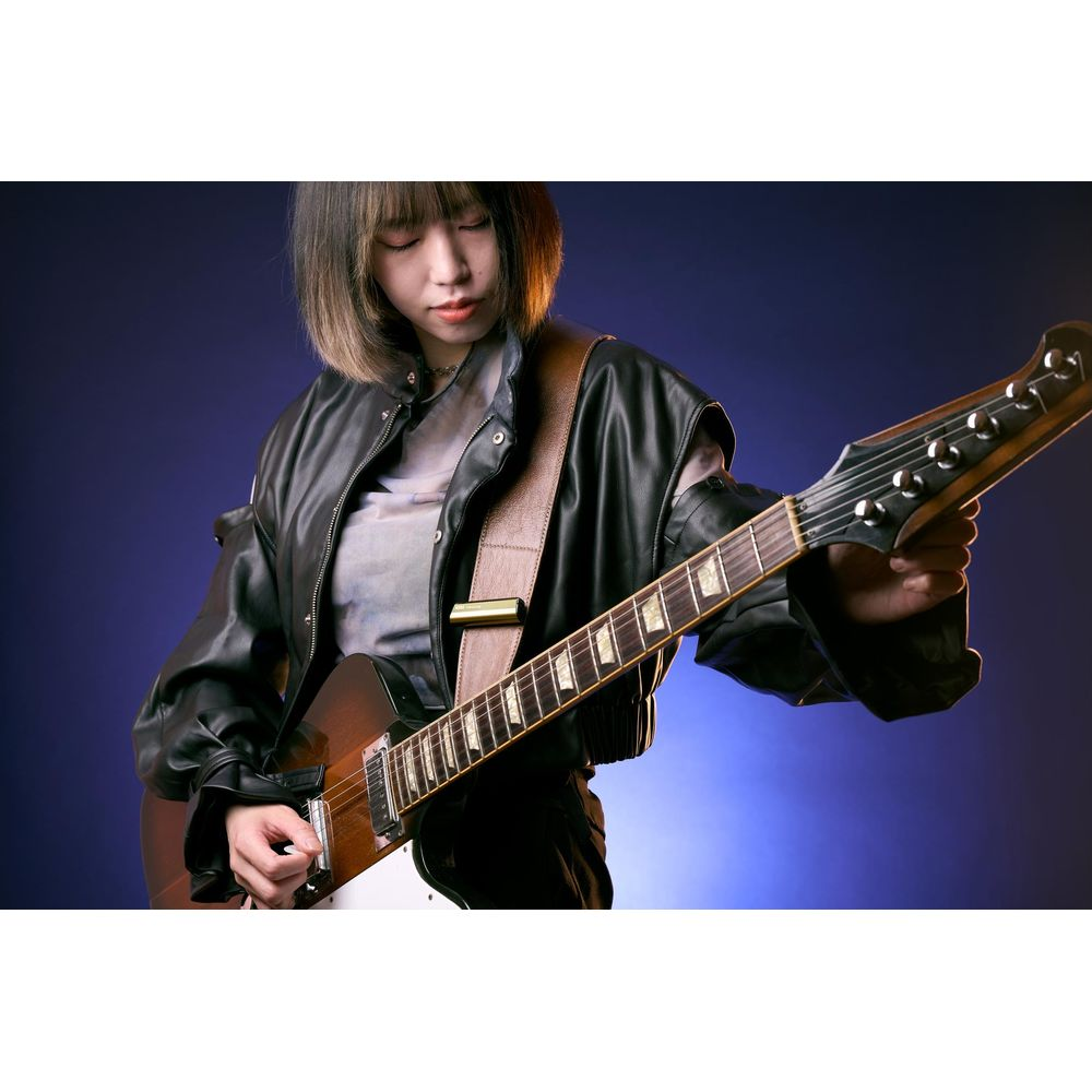 Eine junge Frau mit kurzen Haaren spielt eine braune E-Gitarre vor einem blauen Hintergrund.