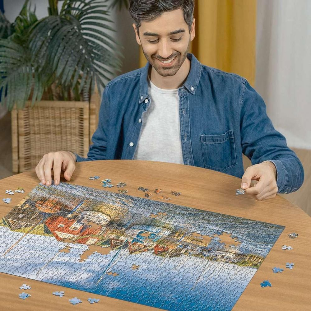 Un homme place une pièce de puzzle dans une scène de ville côtière.