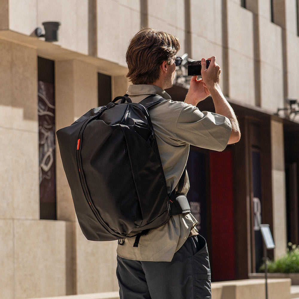 Mann mit schwarzem Rucksack fotografiert mit Kamera in Stadtstraße.
