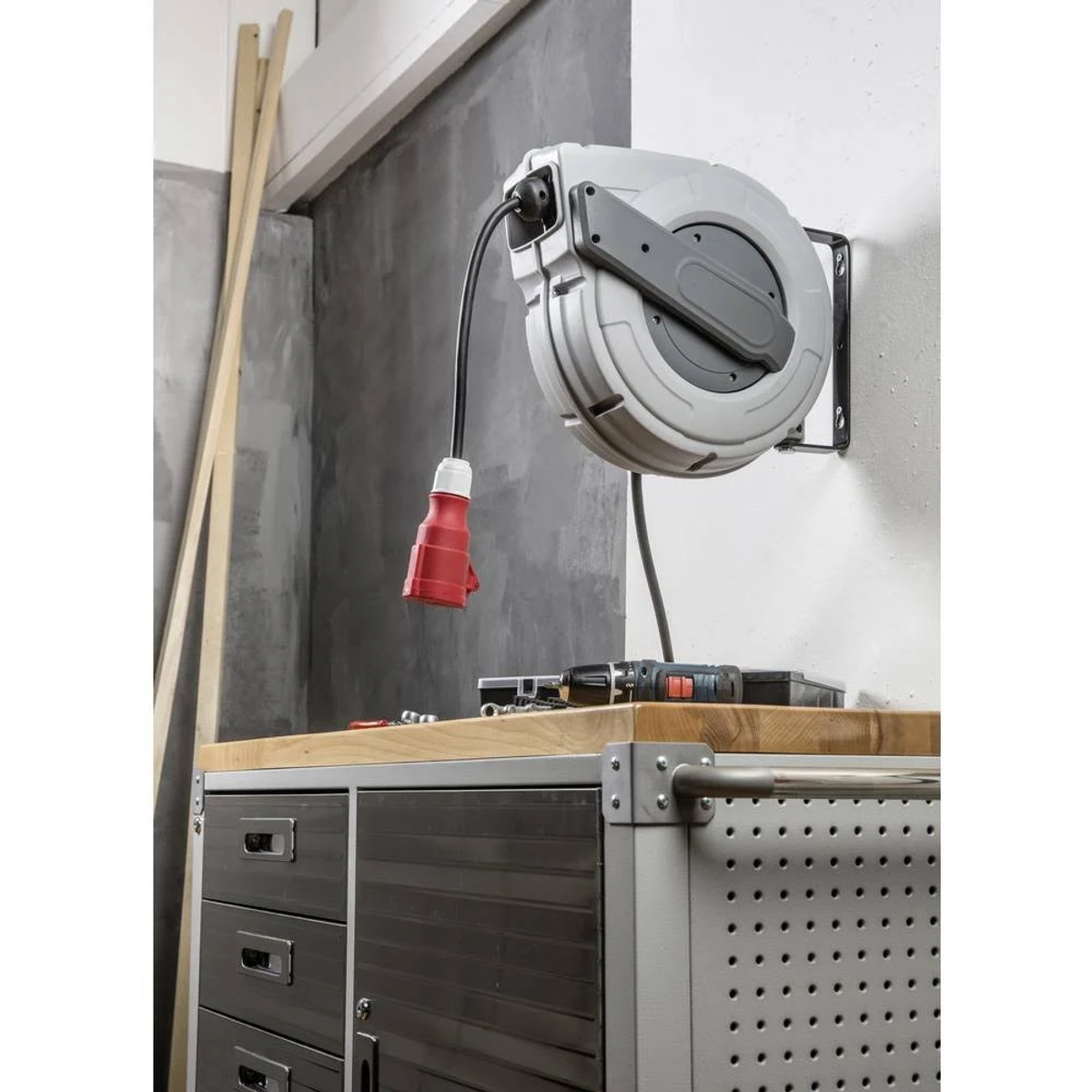 Ein Kabelaufroller mit rotem Stecker hängt über einer Werkbank mit Werkzeugen.