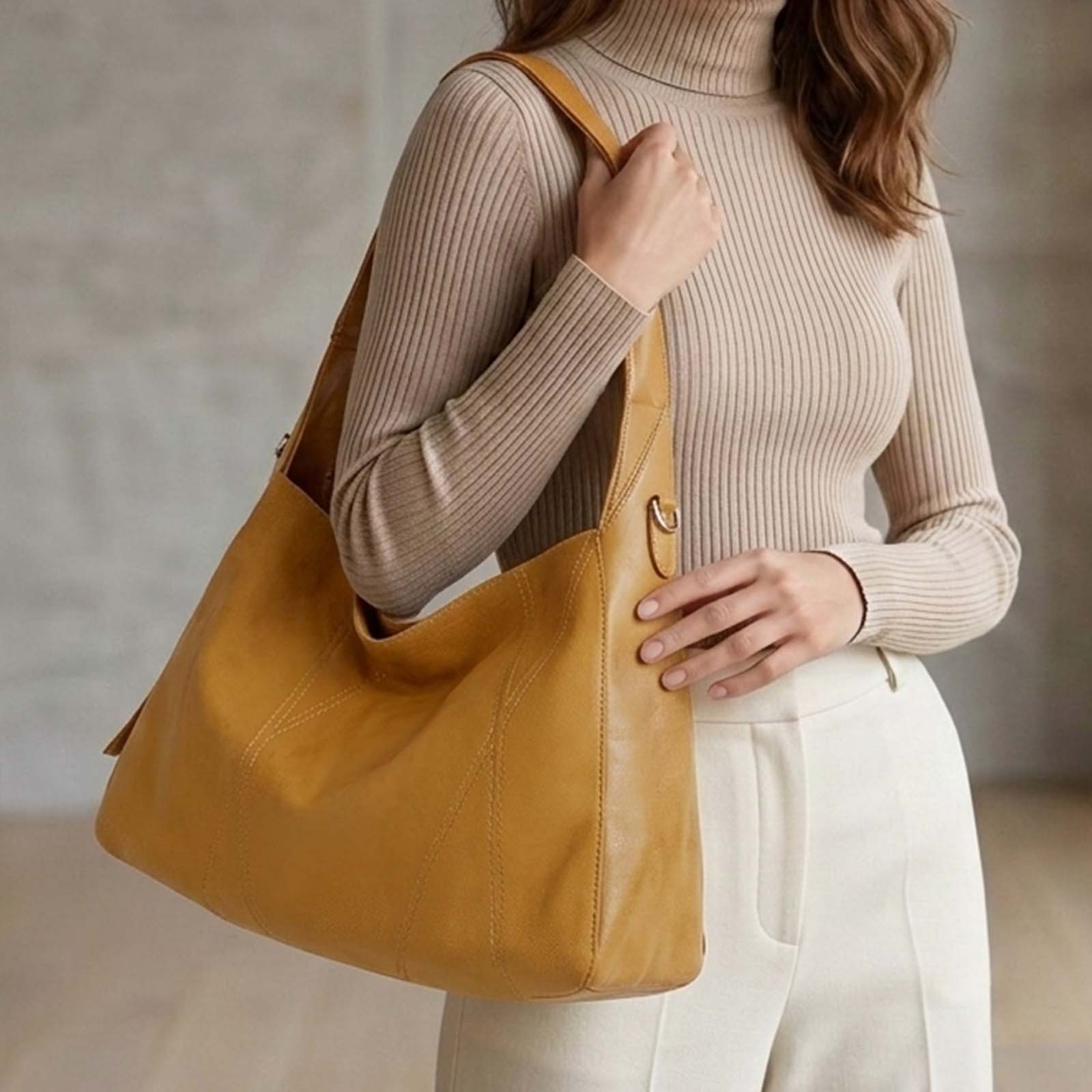 Una mujer con jersey de cuello alto tostado y pantalones blancos lleva un gran bolso de cuero tostado.