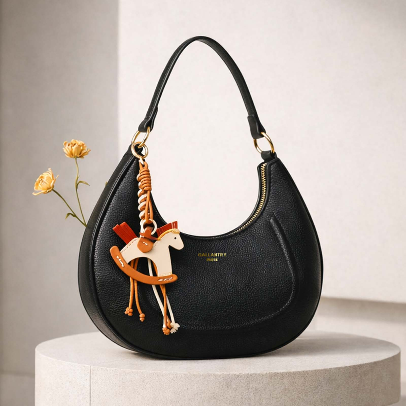 Bolso negro con un charm de caballito balancín y flores al fondo.