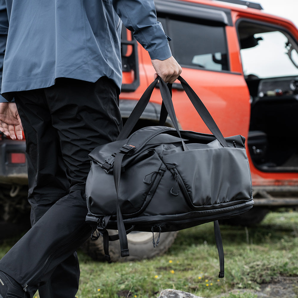 Ein Mann in blauer Jacke trägt eine schwarze Tasche vor einem orangefarbenen Geländewagen.